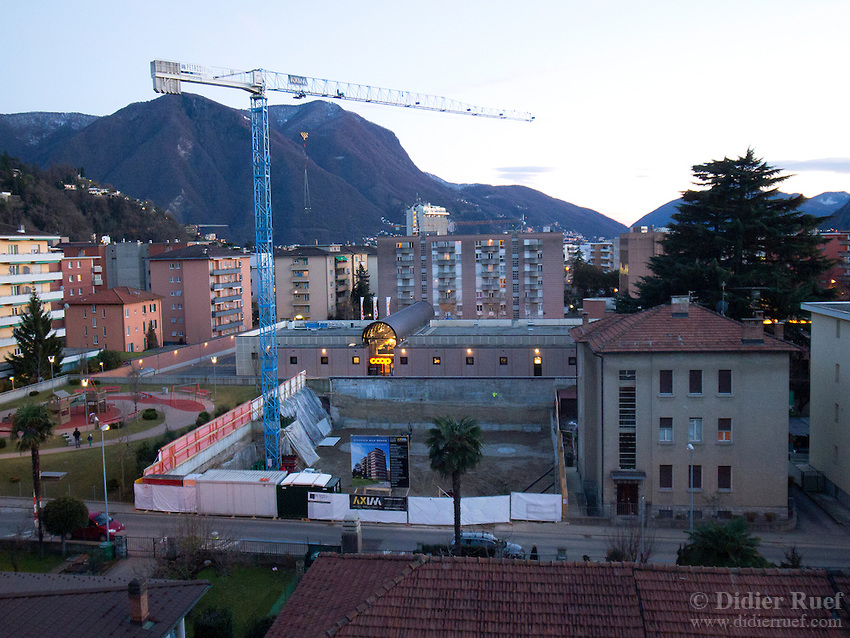 Switzerland. Canton Ticino. Lugano. Construction site for a new house with flats for sale. A supermarket Coop with lights on. Sunset and twilight. 3.02.13 © 2013 Didier Ruef