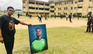 Sylvanus Okwor, Vice President of the Visual Arts and Technology Students Association holds a painted portrait of Nkasi Ford Moses while colleagues play a football game in honor of the late Ford at the Calabar campus of UNICROSS. 29/6/2021
