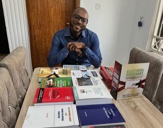 A smiling F. Baba Isa Esq seats at the head of a table with several books on law displayed in front of him